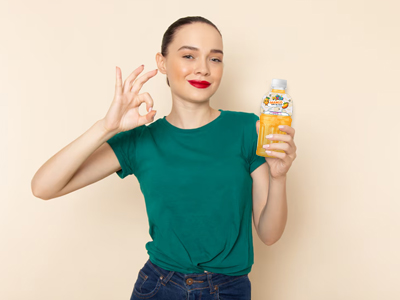 A woman in a green t-shirt holds a yellow bubble tea drink, making an "OK" hand gesture with a smile.